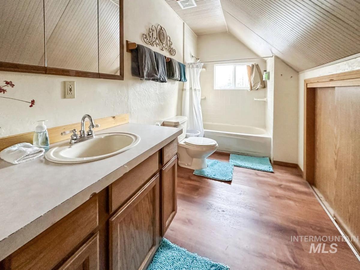 Bathroom featuring vaulted ceiling, wood finished floors, vanity, and shower / tub combo with curtain
