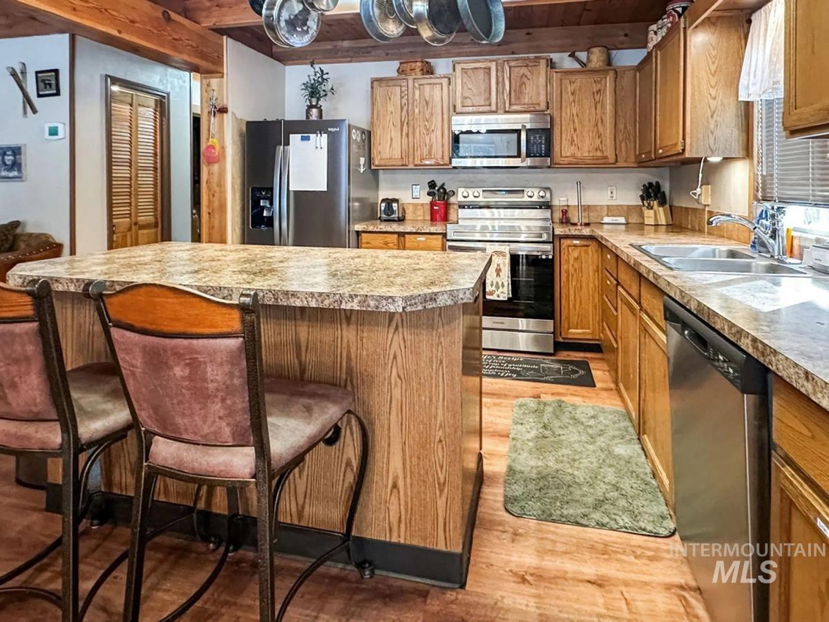 Kitchen with stainless steel appliances, light wood-style floors, beam ceiling, a kitchen island, and light countertops