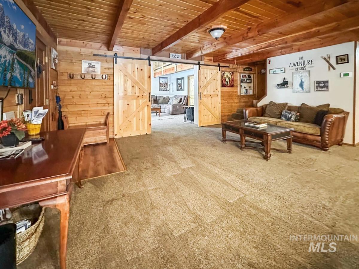 Living area featuring a barn door, a wood ceiling with exposed beams, carpet floors, and wood walls