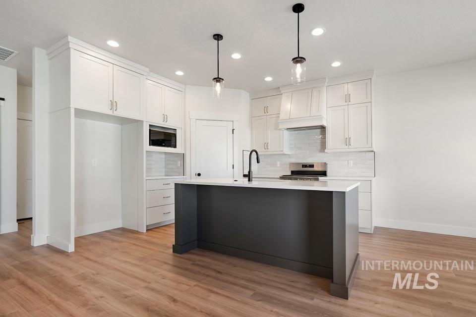 Kitchen with white cabinets, stainless steel range oven, hanging light fixtures, and light wood-type flooring