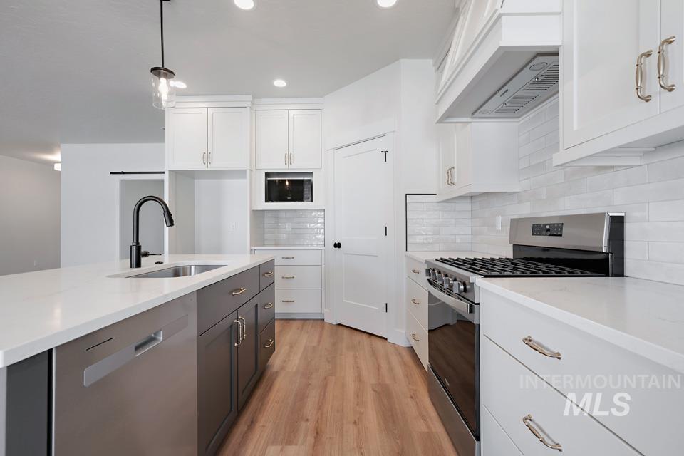Kitchen featuring stainless steel appliances, two tone cabinetry, light wood finished floors, hanging light fixtures, and light stone counters