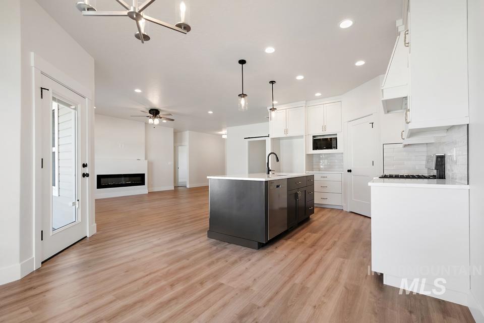 Dual tone kitchen with two tone cabinetry, a glass covered fireplace, a kitchen island with sink, open floor plan, and light wood-style flooring