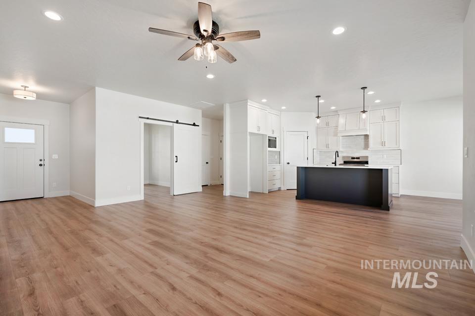 Unfurnished living room featuring a barn door, ceiling fan, recessed lighting, and light wood-type flooring