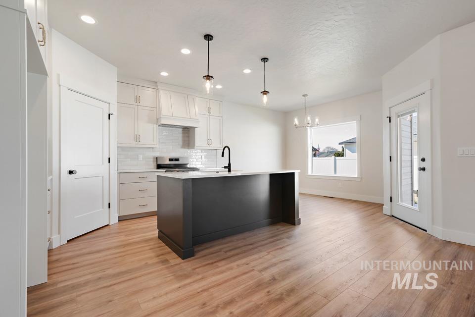 Dual tone kitchen with a center island with sink, light wood finished floors, suspended lighting, decorative backsplash, and two tone cabinets