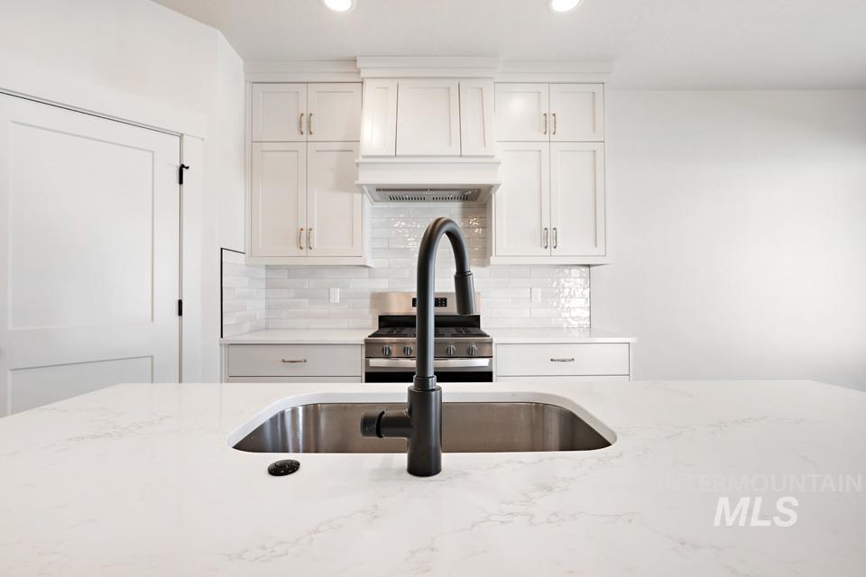 Kitchen featuring light stone countertops, gas range, white cabinetry, tasteful backsplash, and recessed lighting