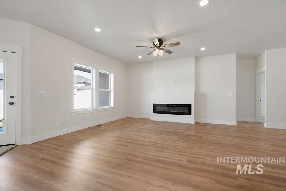 Unfurnished living room with ceiling fan, light wood finished floors, a glass covered fireplace, and recessed lighting