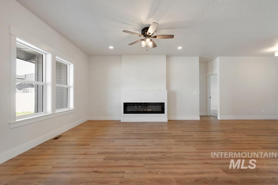 Unfurnished living room featuring a ceiling fan, light wood-type flooring, a glass covered fireplace, and recessed lighting