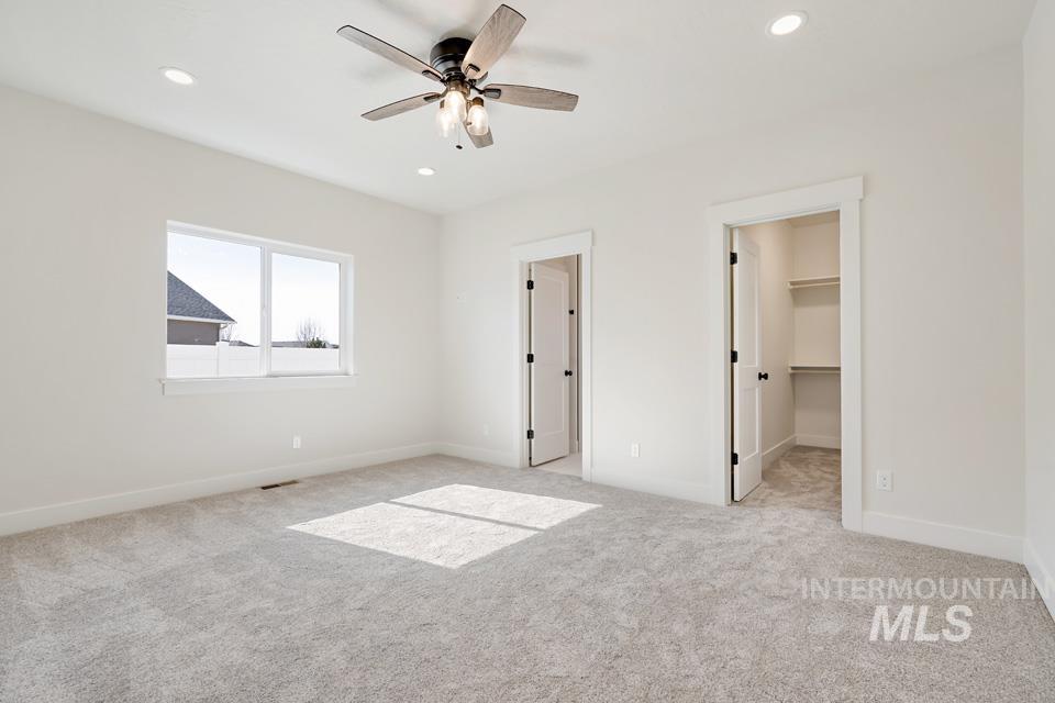Unfurnished bedroom with light colored carpet, a walk in closet, ceiling fan, and recessed lighting