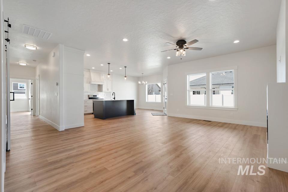 Unfurnished living room featuring light wood-style flooring, a ceiling fan, and a chandelier