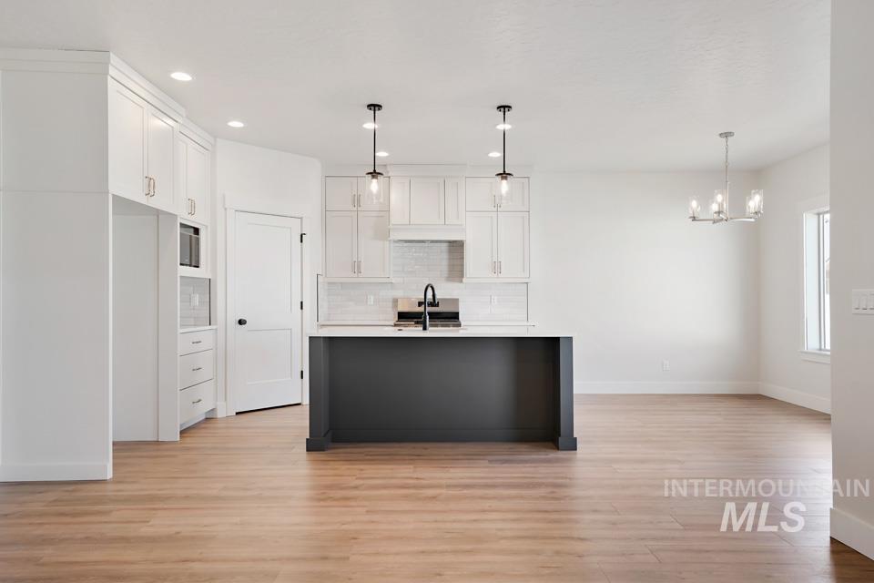 Kitchen with white cabinets, light wood-style floors, suspended lighting, and an island with sink