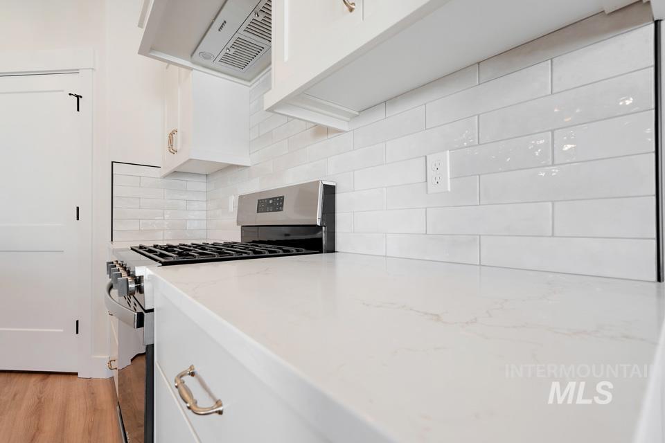 Kitchen with gas stove, white cabinetry, extractor fan, light wood-style flooring, and light stone counters
