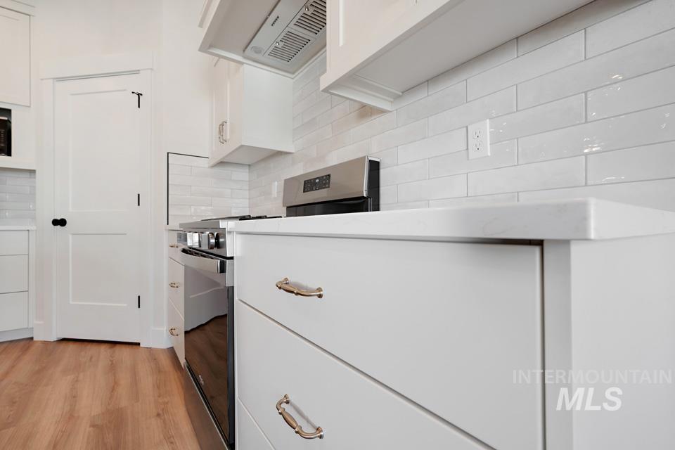 Kitchen featuring stainless steel range with gas stovetop, exhaust hood, light wood-style floors, white cabinets, and decorative backsplash