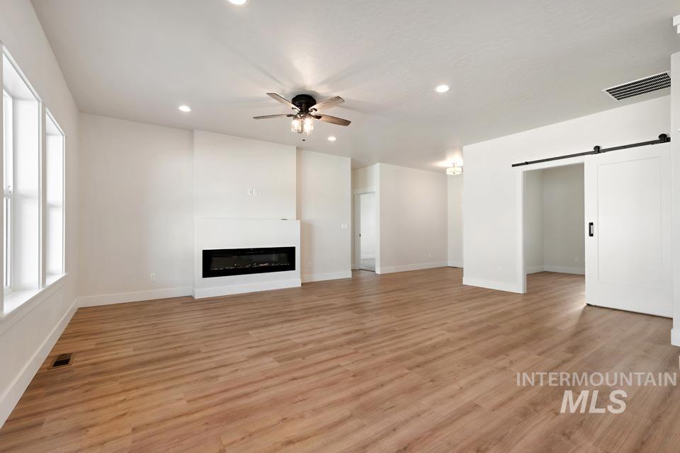 Unfurnished living room featuring a barn door, ceiling fan, light wood finished floors, a glass covered fireplace, and recessed lighting