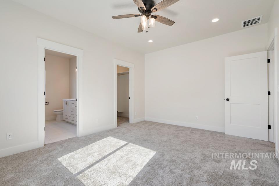 Unfurnished bedroom with a walk in closet, light colored carpet, ceiling fan, ensuite bathroom, and recessed lighting