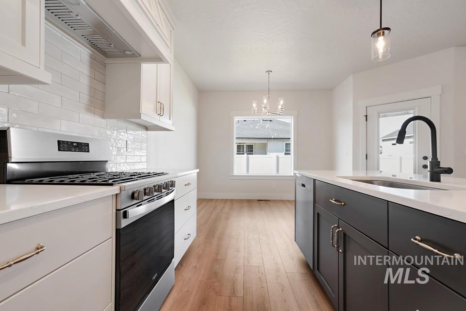 Kitchen with stainless steel appliances, backsplash, two tone color scheme, light wood-style flooring, and light stone counters