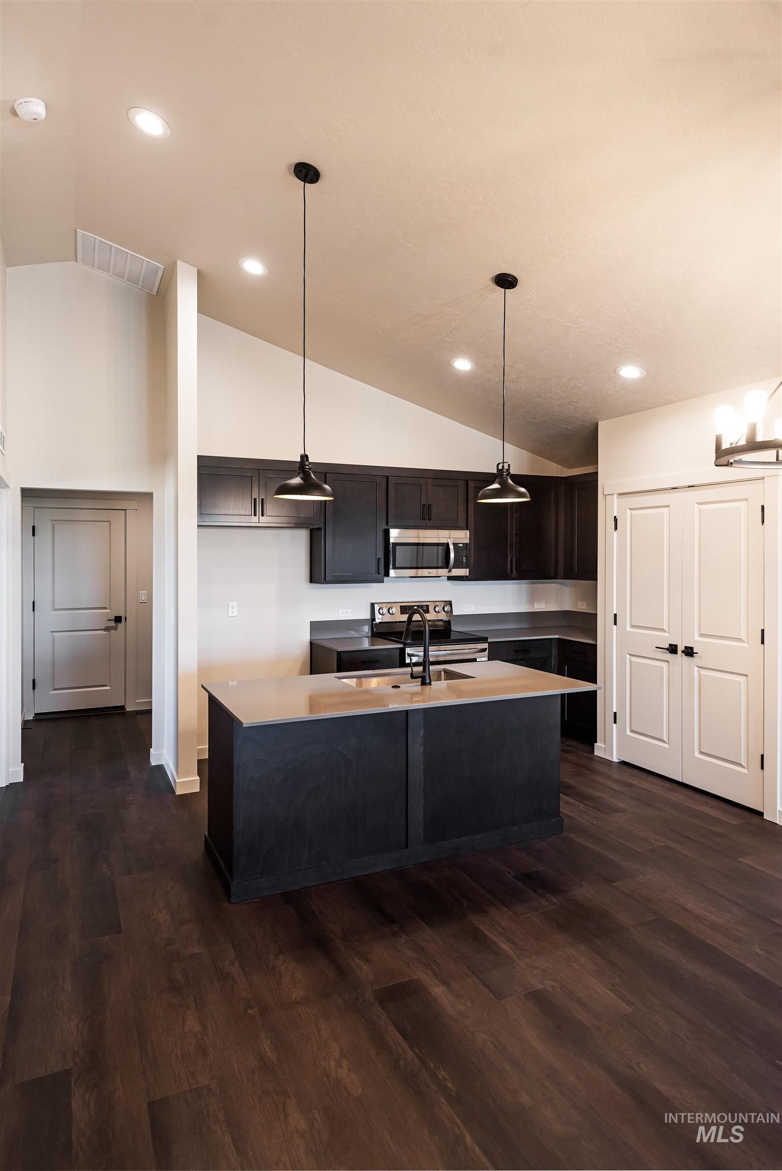 Kitchen featuring lofted ceiling, pendant lighting, dark wood-type flooring, stainless steel appliances, and recessed lighting