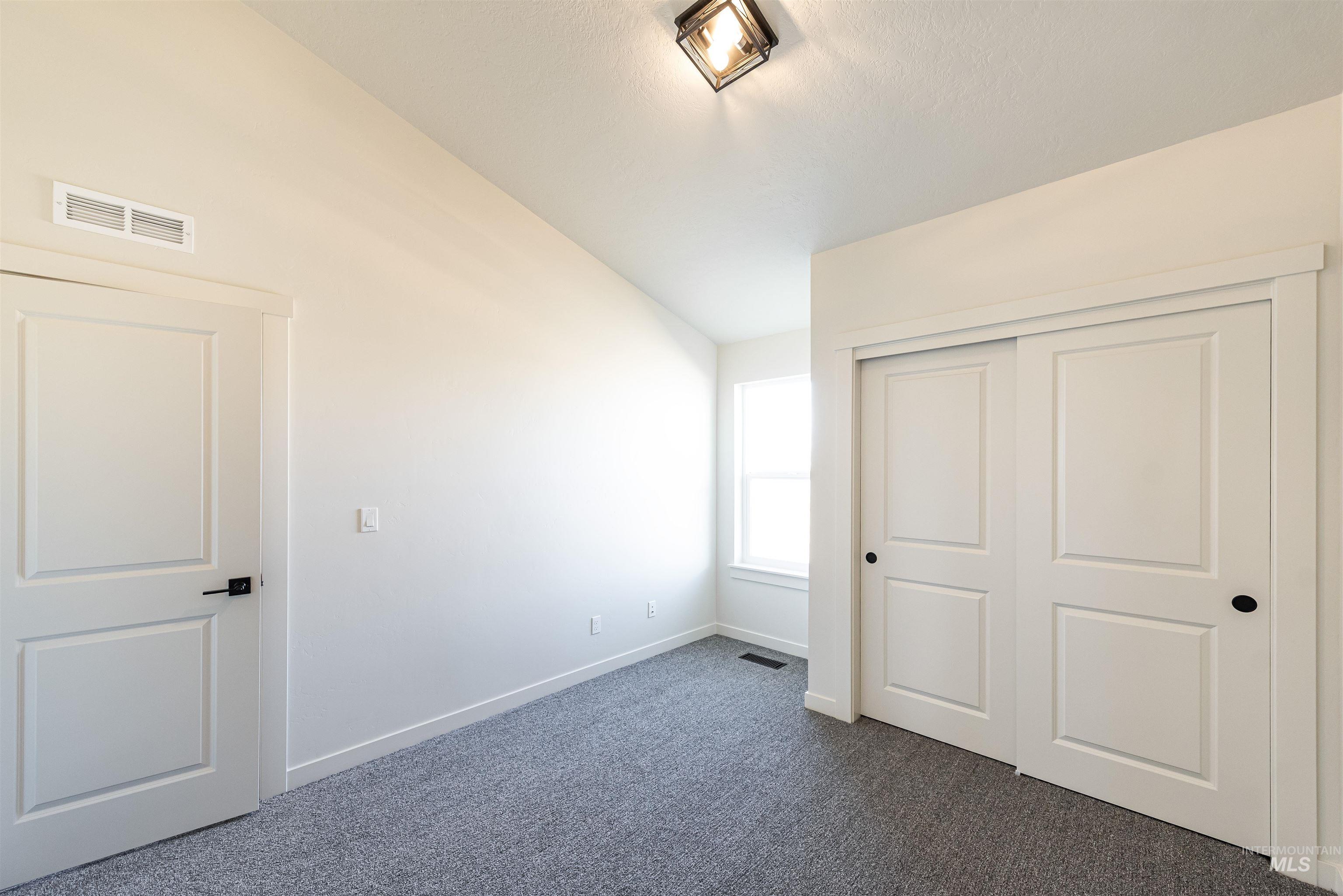 Unfurnished bedroom with dark colored carpet, a closet, and vaulted ceiling