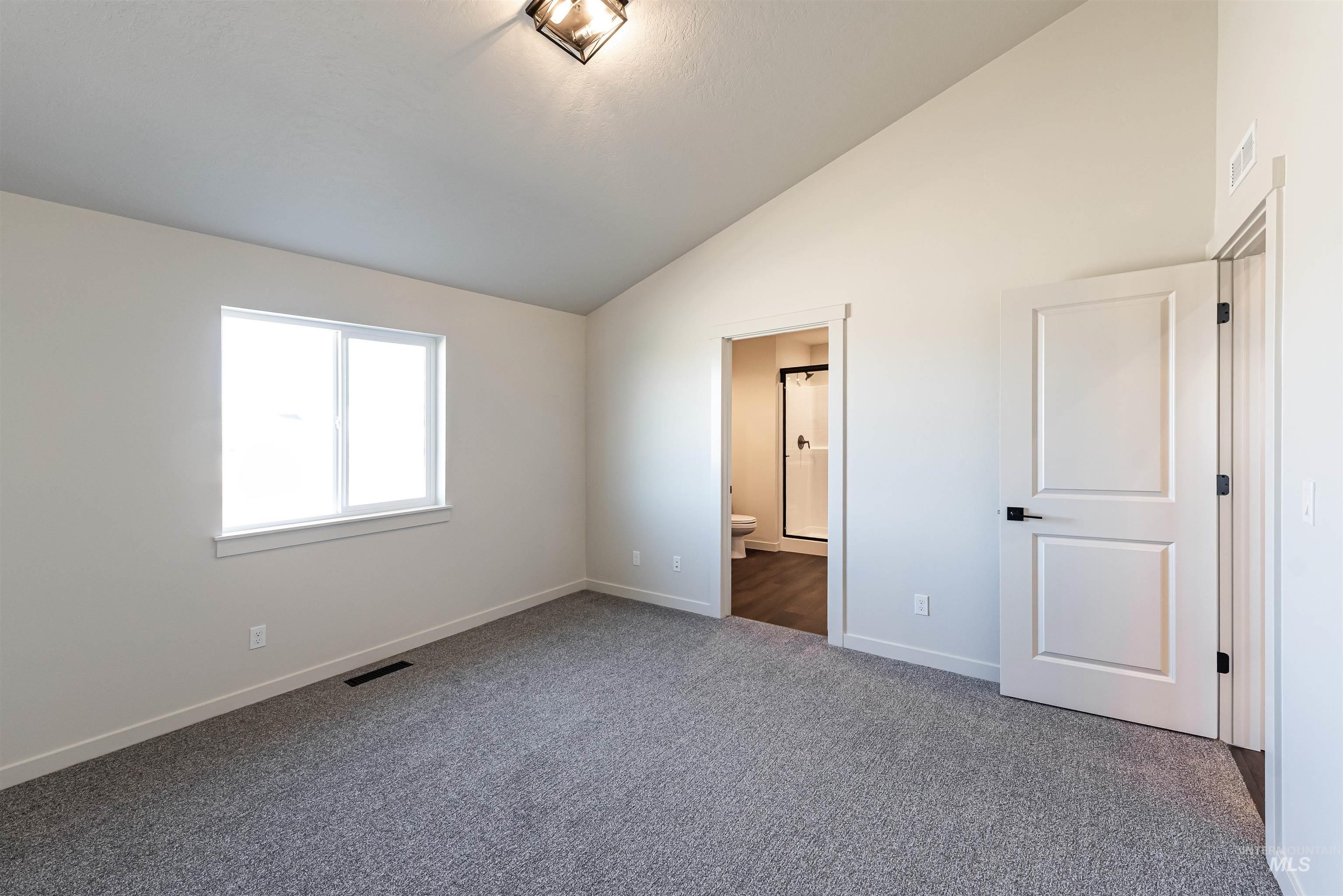 Unfurnished bedroom featuring ensuite bath, carpet, and high vaulted ceiling