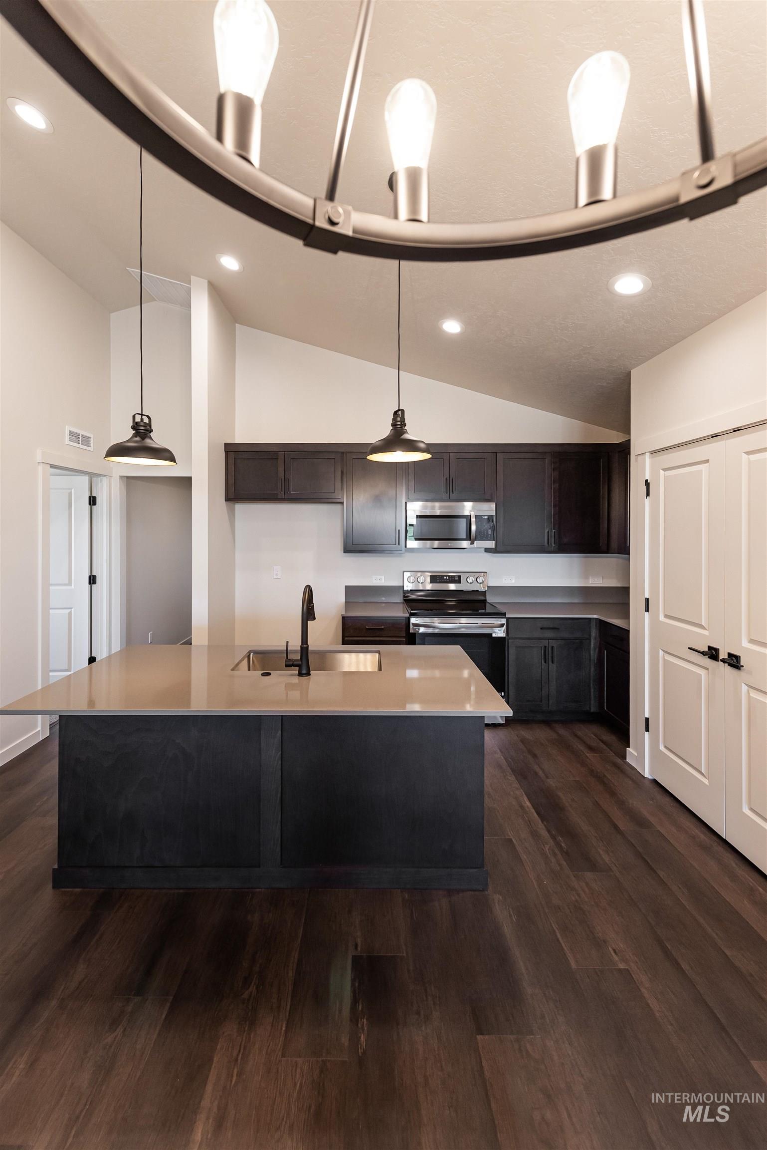 Kitchen with vaulted ceiling, stainless steel appliances, dark wood-style floors, hanging light fixtures, and dark brown cabinetry