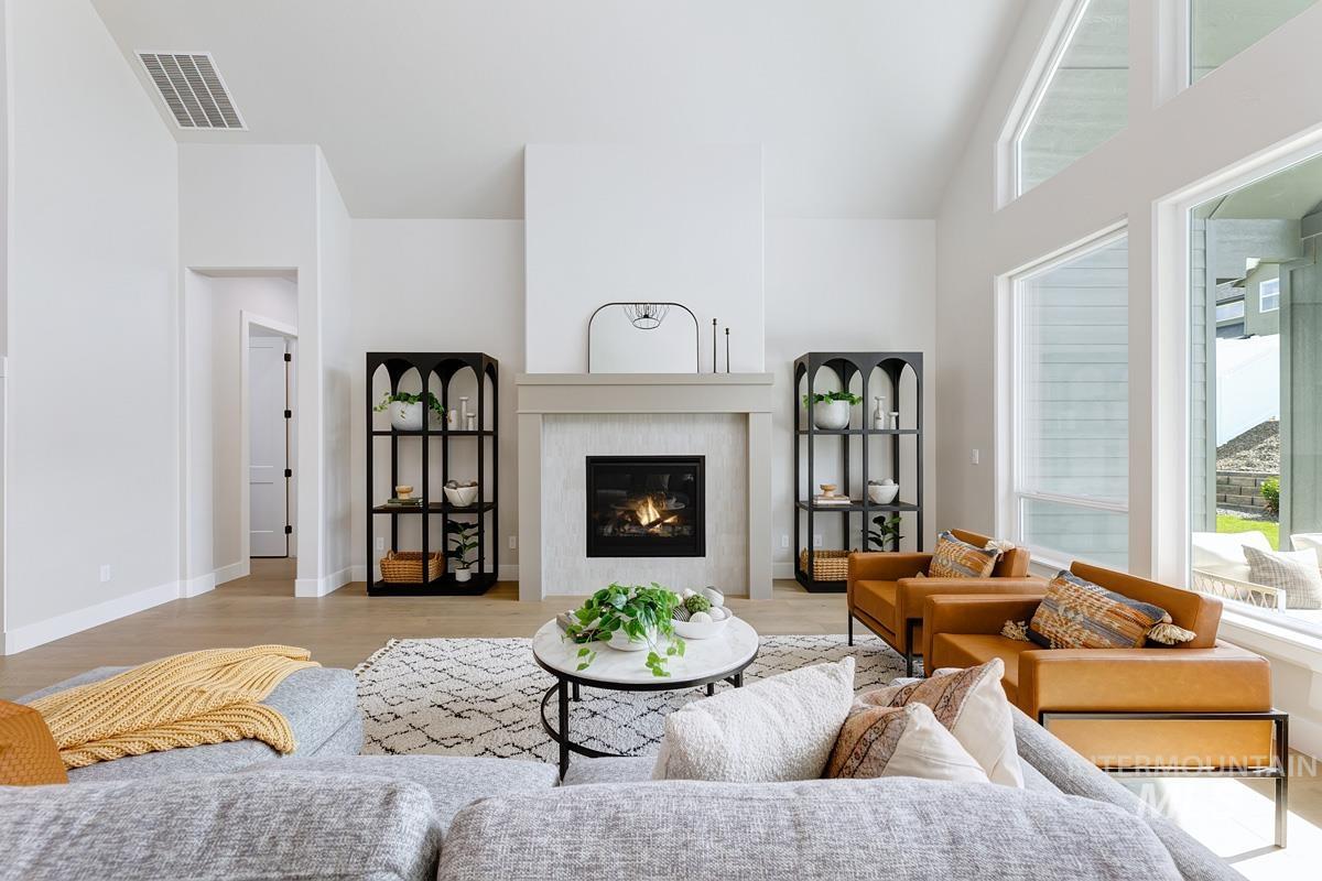 Living area featuring healthy amount of natural light, a glass covered fireplace, a high ceiling, and wood finished floors