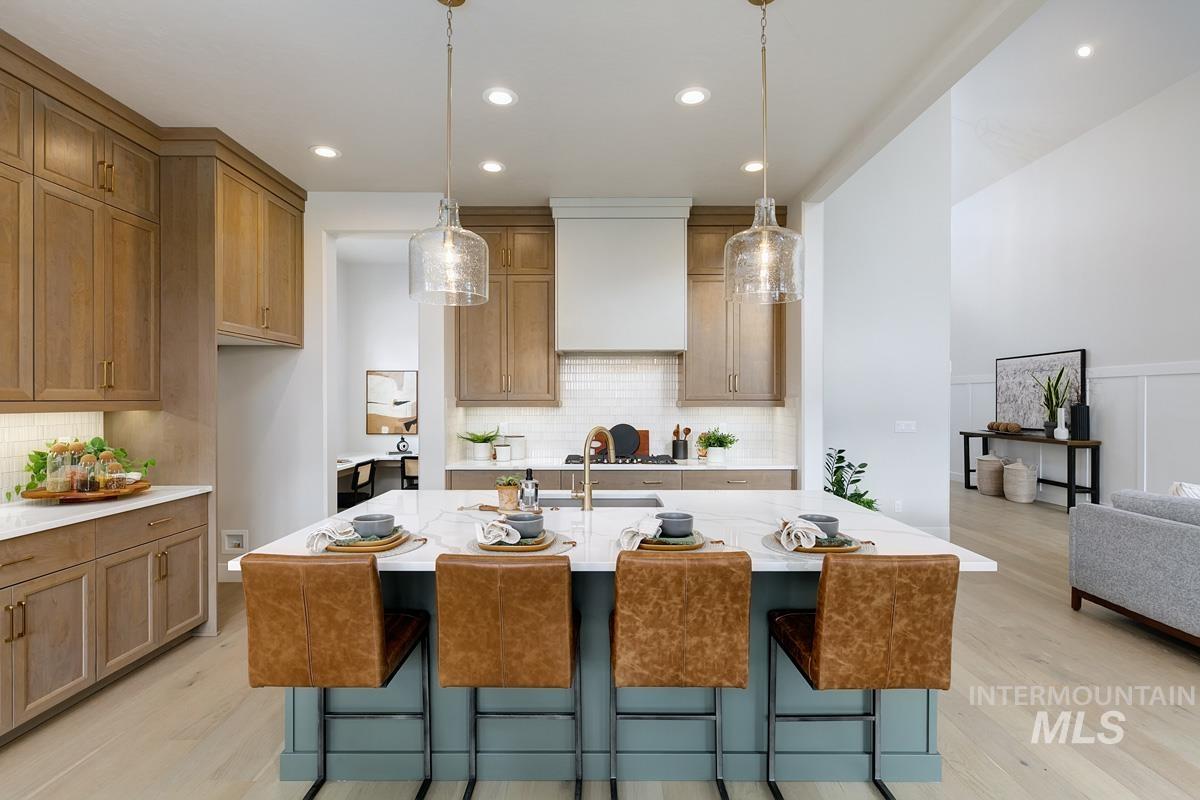Kitchen with a kitchen bar, backsplash, hanging light fixtures, an island with sink, and recessed lighting