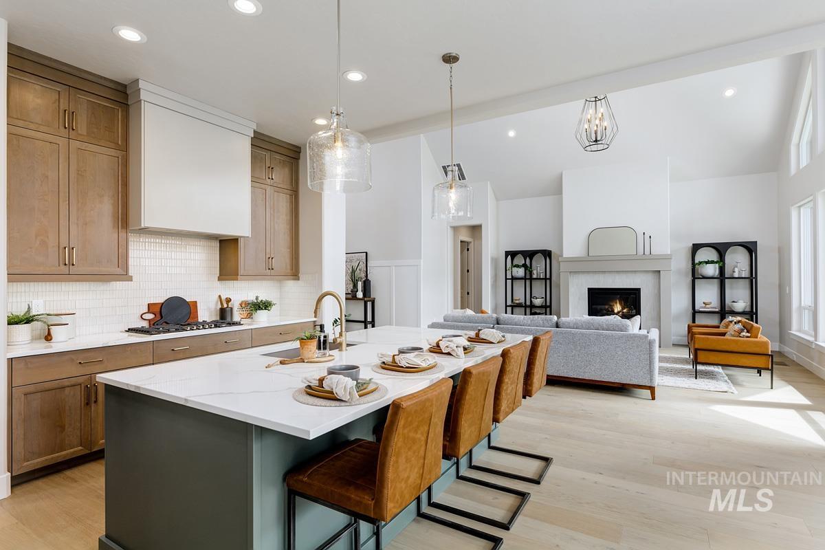 Kitchen with a kitchen breakfast bar, a center island with sink, light wood-style floors, a warm lit fireplace, and light stone counters
