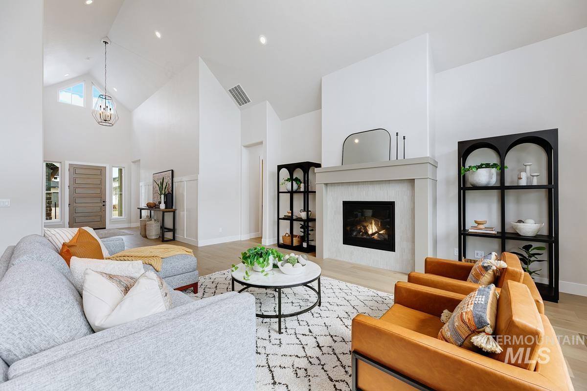 Living area with high vaulted ceiling, light wood-style floors, a glass covered fireplace, and a chandelier
