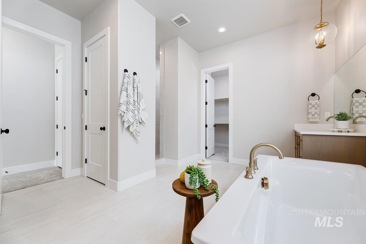 Full bath featuring vanity, a soaking tub, a spacious closet, and recessed lighting