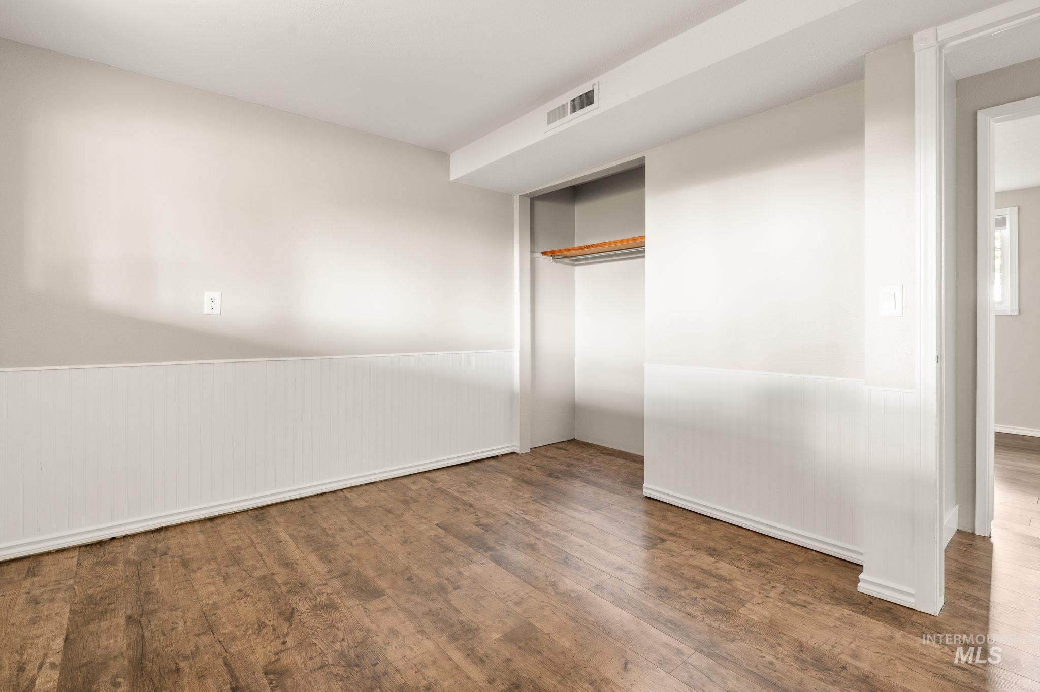 Unfurnished bedroom with wood finished floors, a closet, and a wainscoted wall