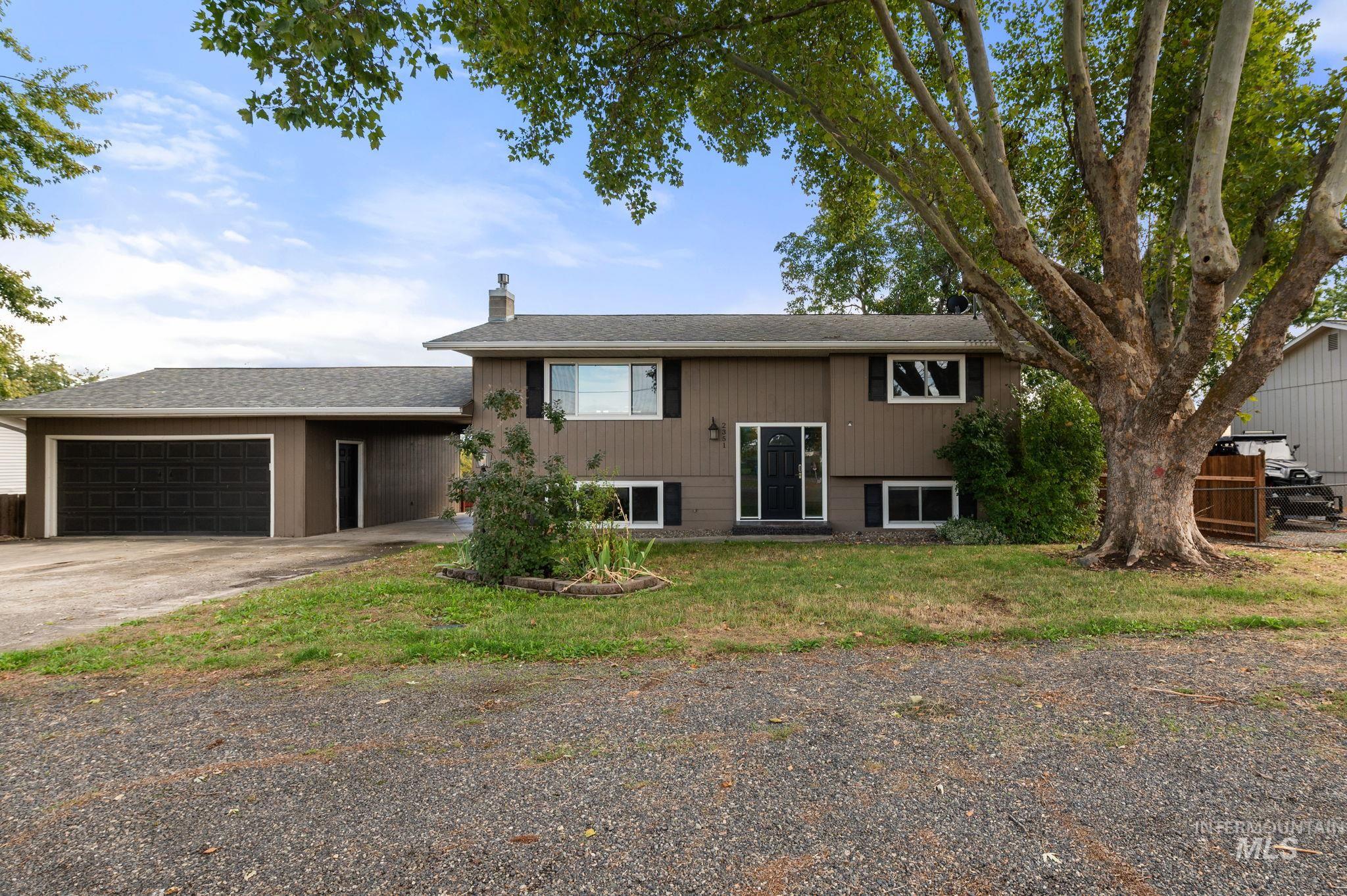 Split foyer home featuring a chimney, concrete driveway, a garage, roof with shingles, and a front lawn