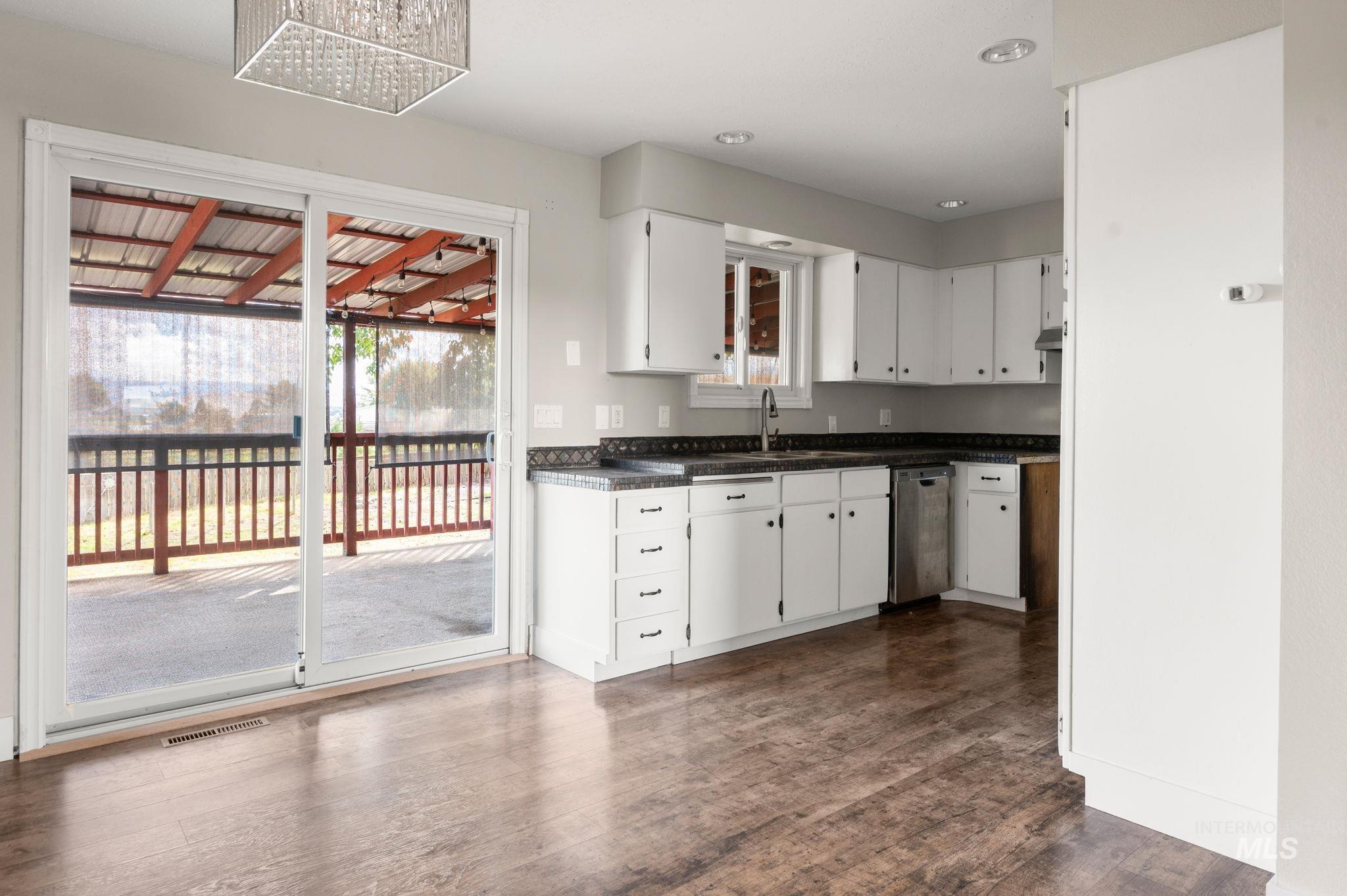 Kitchen featuring white cabinetry, dark countertops, dark wood-style floors, dishwasher, and a chandelier