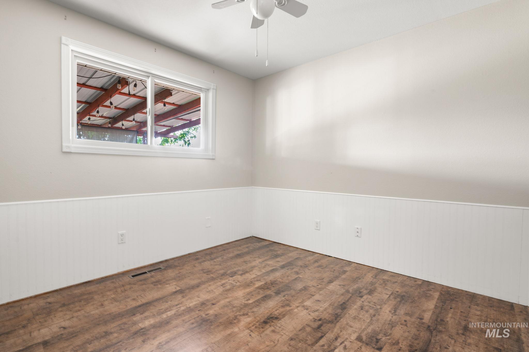 Empty room featuring wood finished floors, wainscoting, and ceiling fan