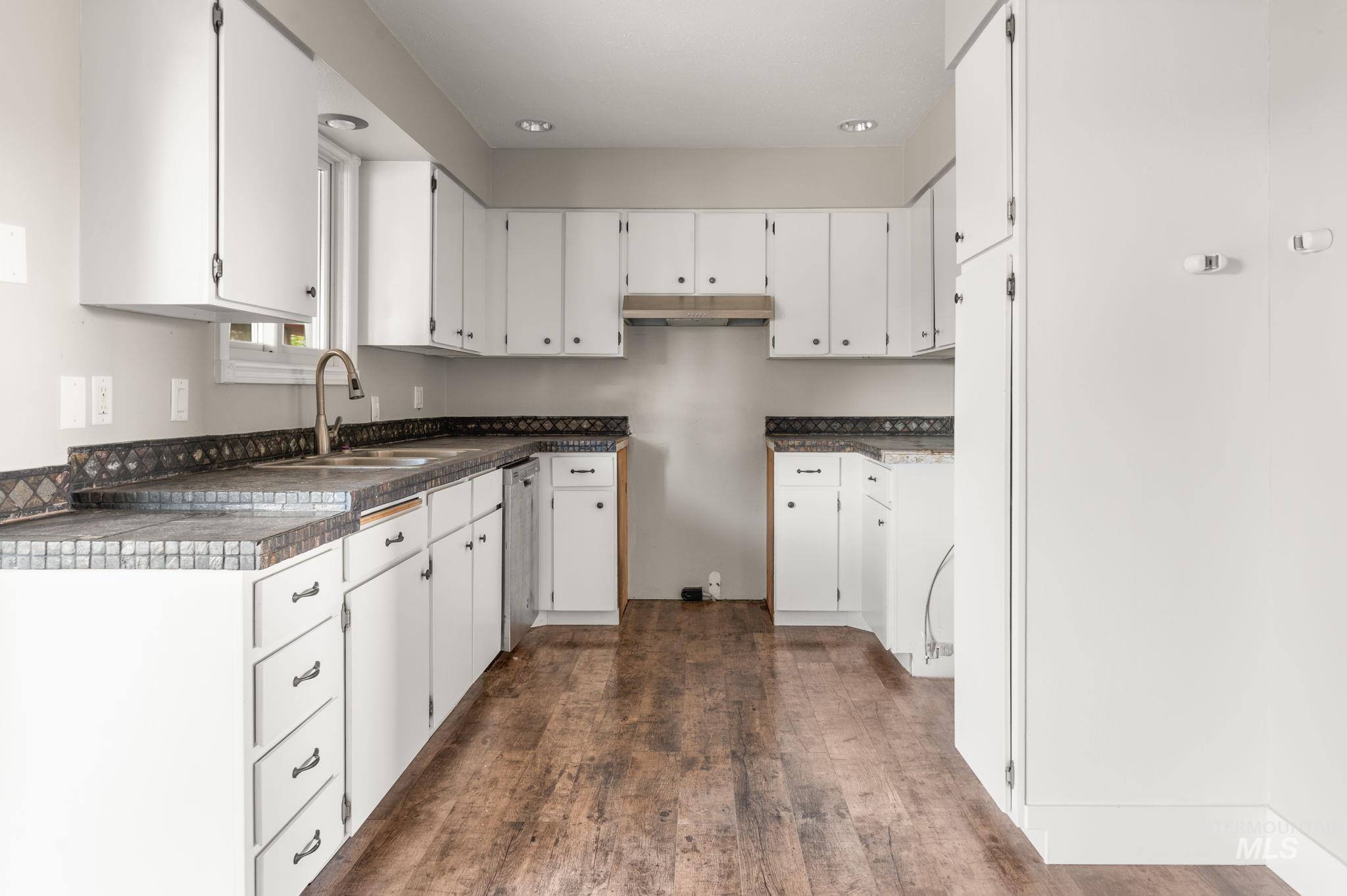 Kitchen with white cabinetry, dark wood-type flooring, dark countertops, under cabinet range hood, and recessed lighting