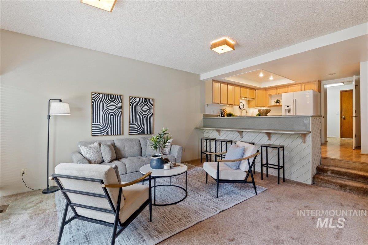 Living area with a kitchen pass-through featuring natural wood cabinetry, a breakfast bar, and a double-basin stainless steel sink