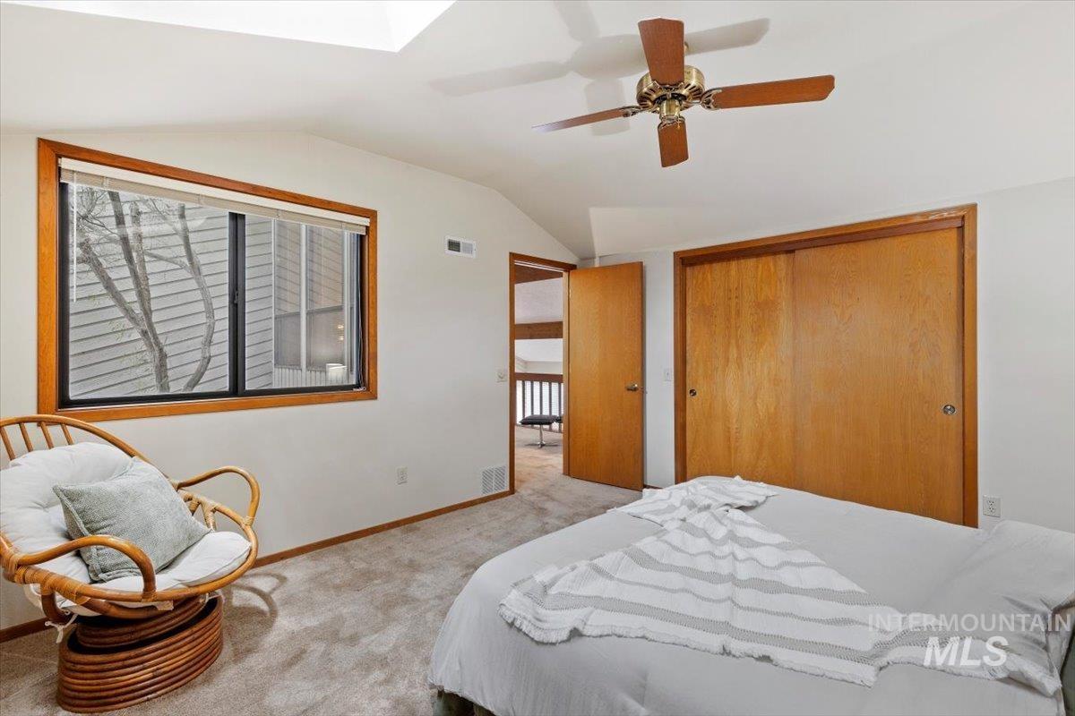 Carpeted room featuring a skylight, sloped ceiling, wood-finish window trim, and sliding closet doors
