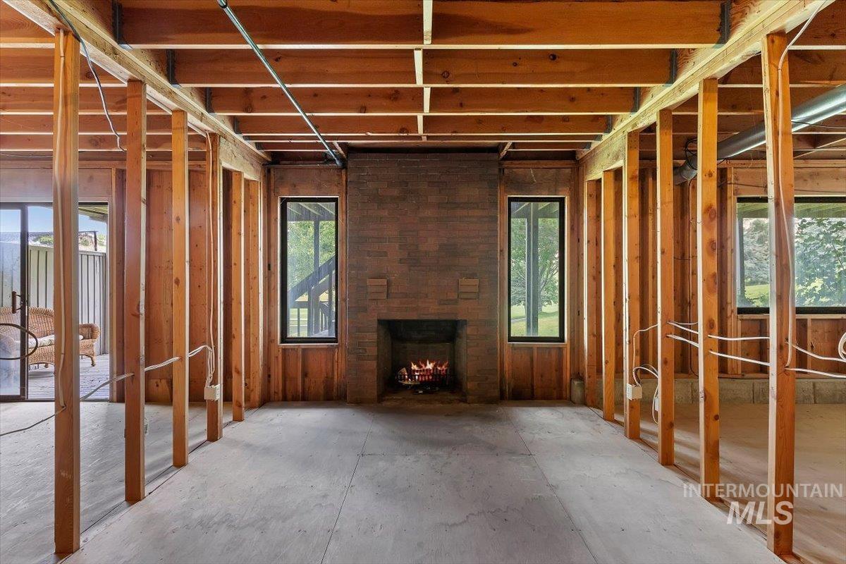 Unfinished interior space featuring exposed wood framing, a brick fireplace, two vertical windows, an exposed wood plank ceiling, and concrete flooring