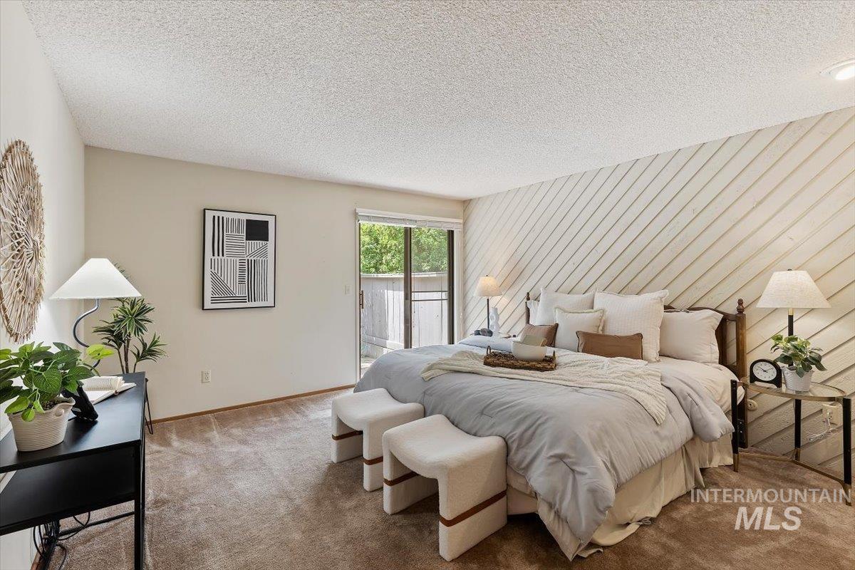 Bedroom featuring a textured accent wall with diagonal paneling, neutral-tone carpeting, and a sliding glass door providing natural light
