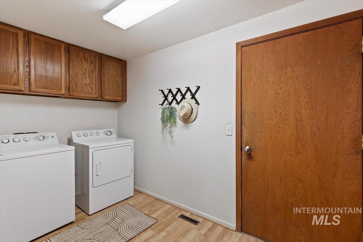 Dedicated laundry space featuring wood-finish flooring, overhead cabinetry, and a full-size washer and dryer