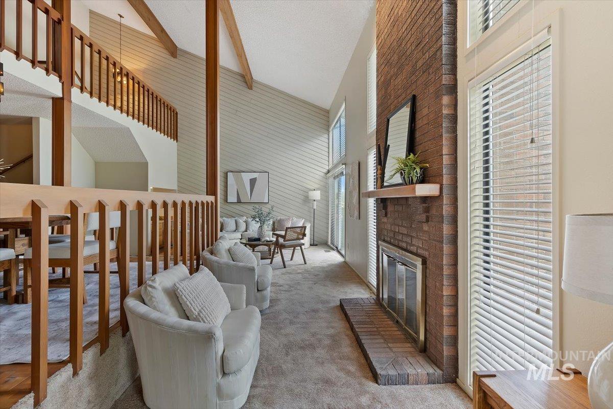 Living area featuring a brick fireplace with a wood mantle, vaulted ceilings with wood beams, and a wood-finish railing