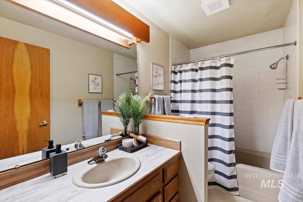 Bathroom featuring a white bathtub with tile surround, wood-finish vanity with an integrated sink, and a large mirror with overhead lighting