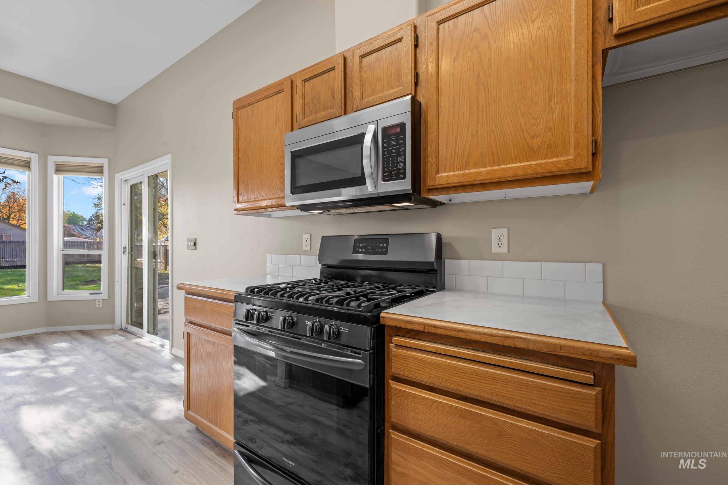 Kitchen with gas stove, light countertops, stainless steel microwave, and light wood-type flooring