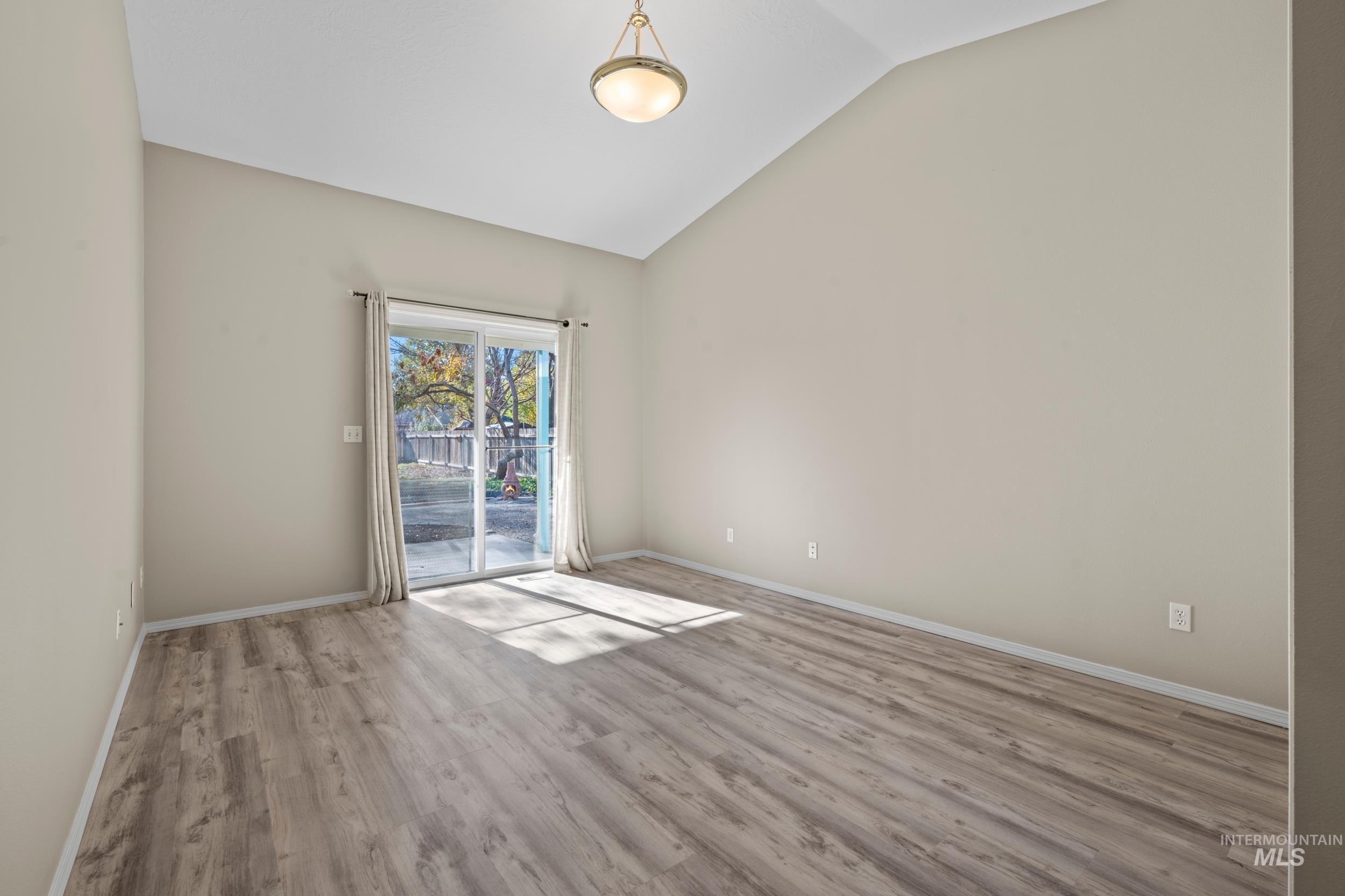 Empty room with light wood-style flooring, vaulted ceiling, and glass sliding door