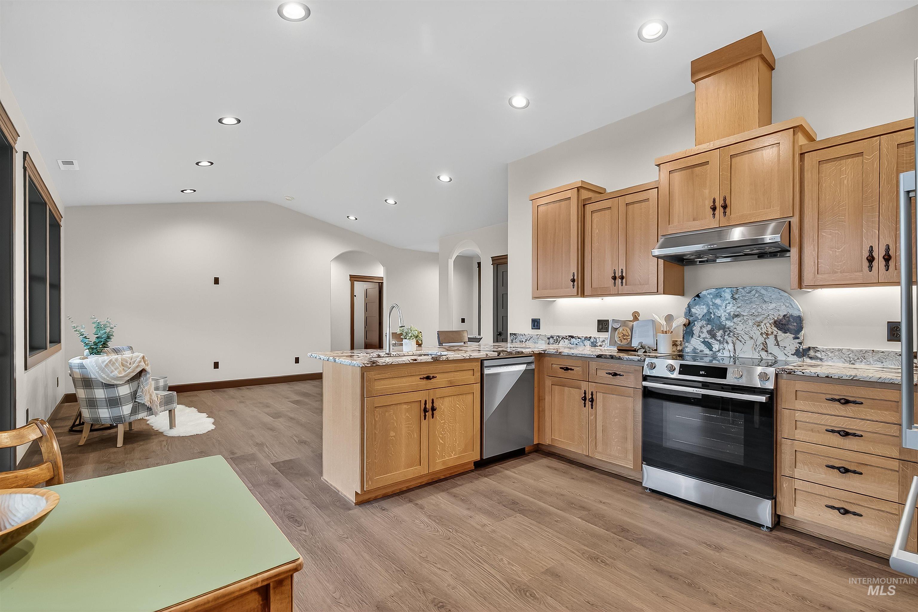 Kitchen featuring arched walkways, lofted ceiling, appliances with stainless steel finishes, light stone countertops, and light wood-style floors