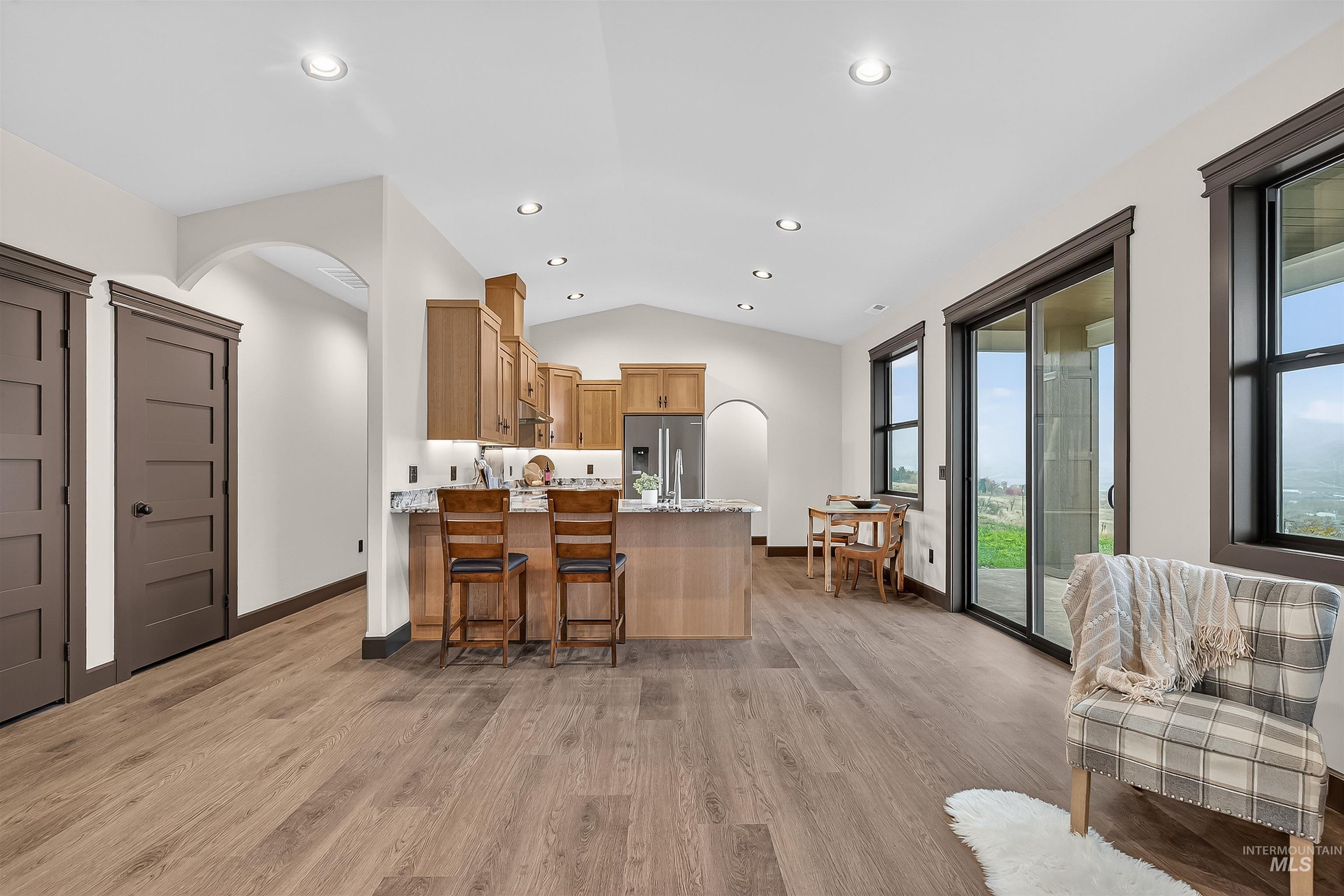 Kitchen with arched walkways, a peninsula, lofted ceiling, a kitchen bar, and light wood finished floors