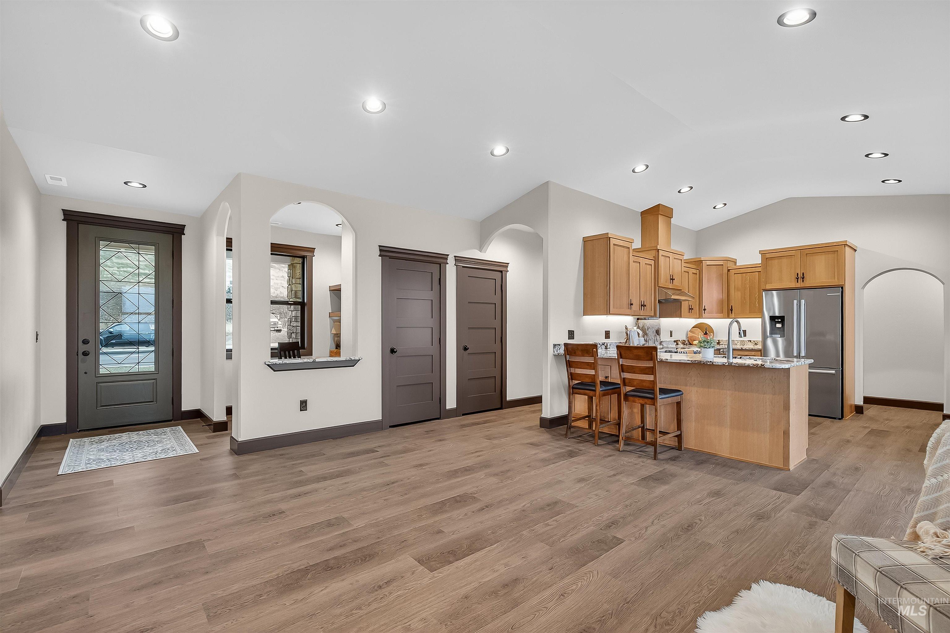 Kitchen with arched walkways, a peninsula, stainless steel fridge, light wood-style flooring, and light stone countertops