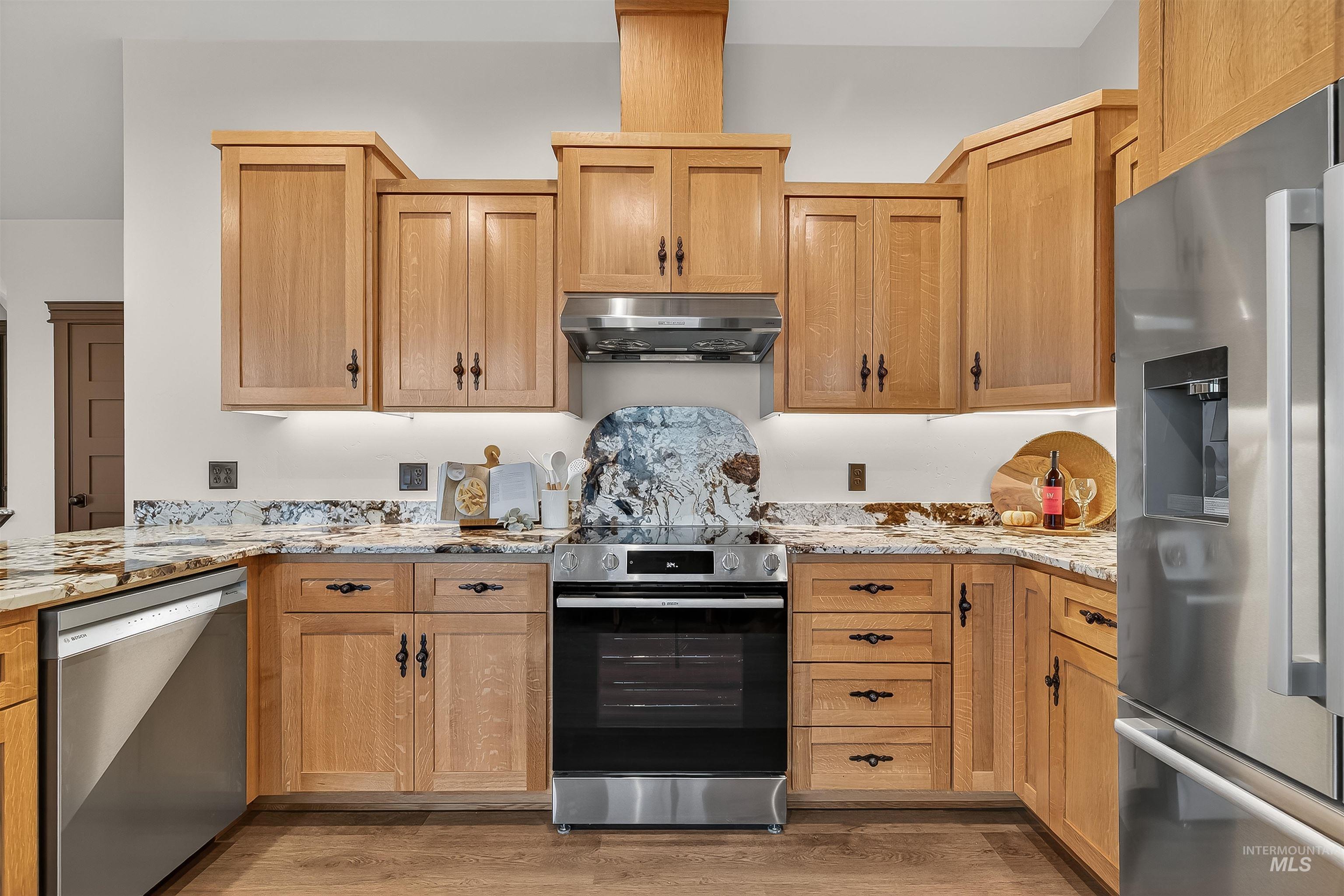 Kitchen featuring stainless steel appliances, light stone countertops, extractor fan, and light wood-style floors