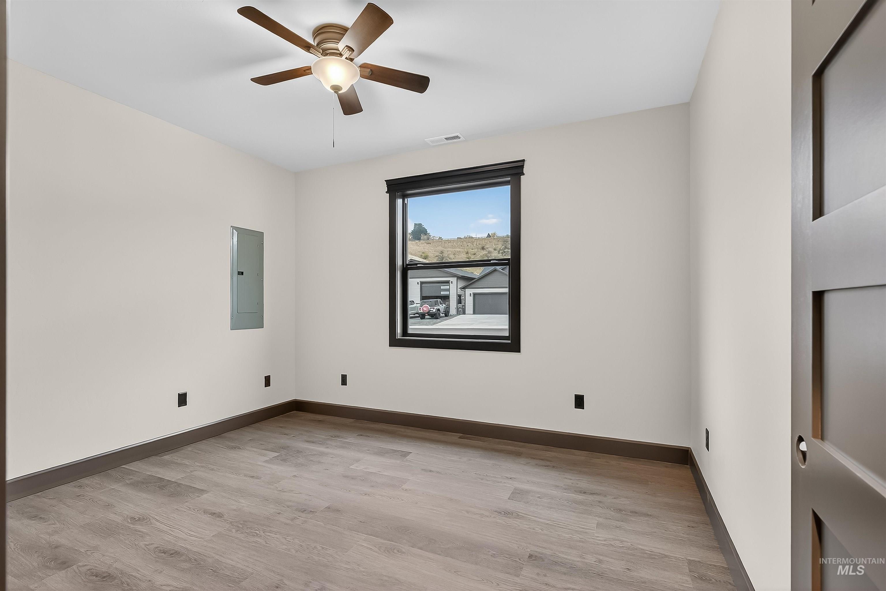 Unfurnished room with light wood-style floors, electric panel, and ceiling fan