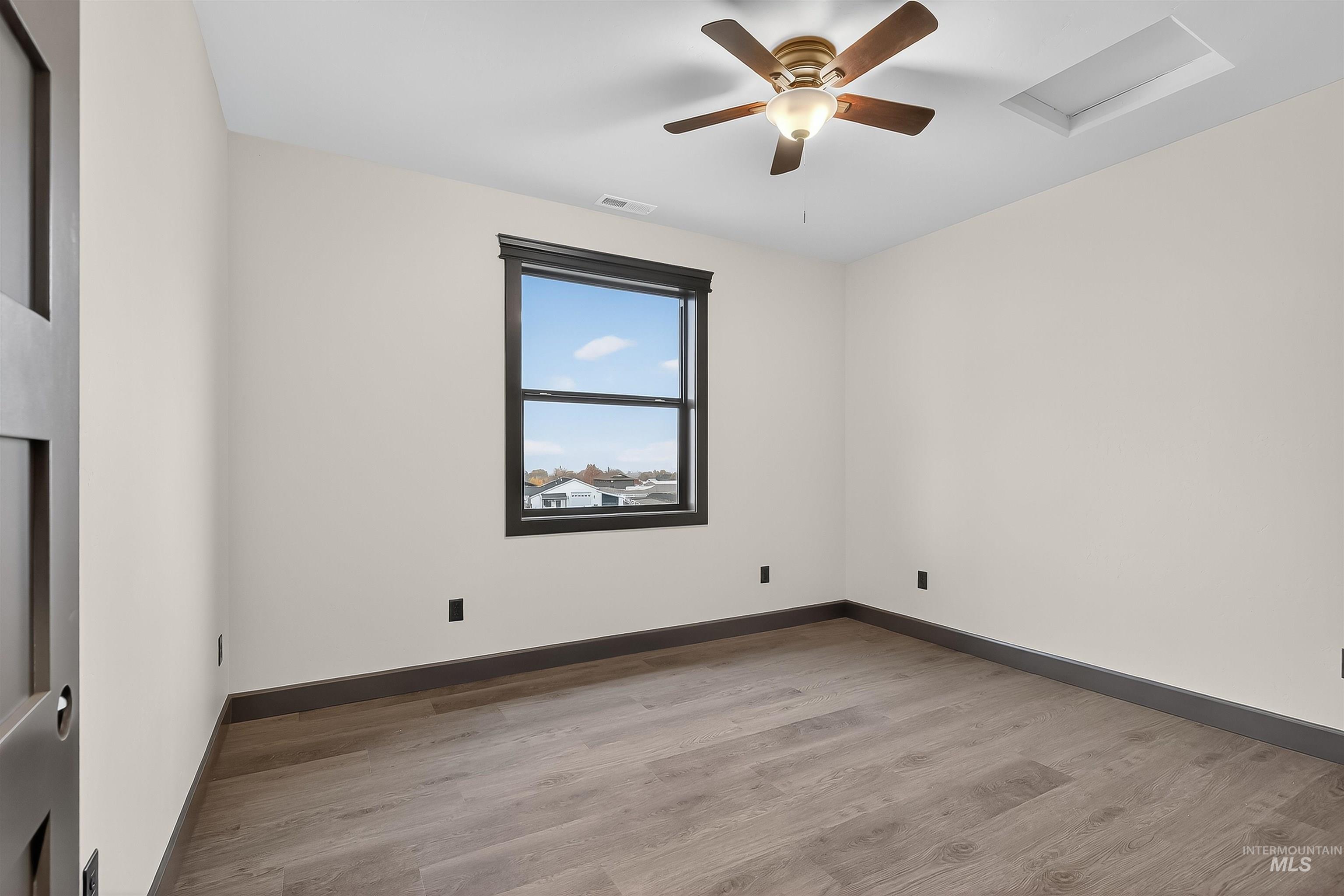 Empty room with attic access, light wood finished floors, and a ceiling fan