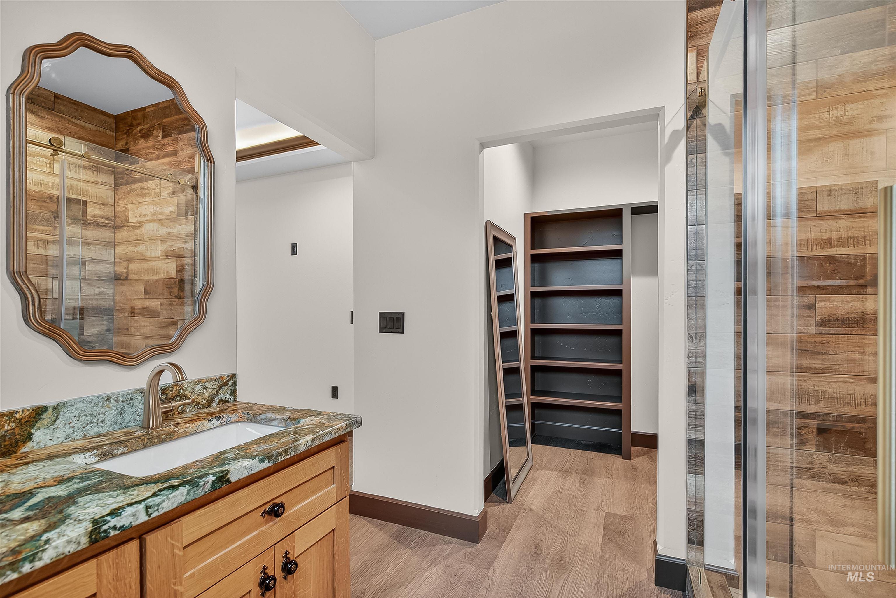 Full bathroom with vanity, light wood-type flooring, a spacious closet, and a stall shower