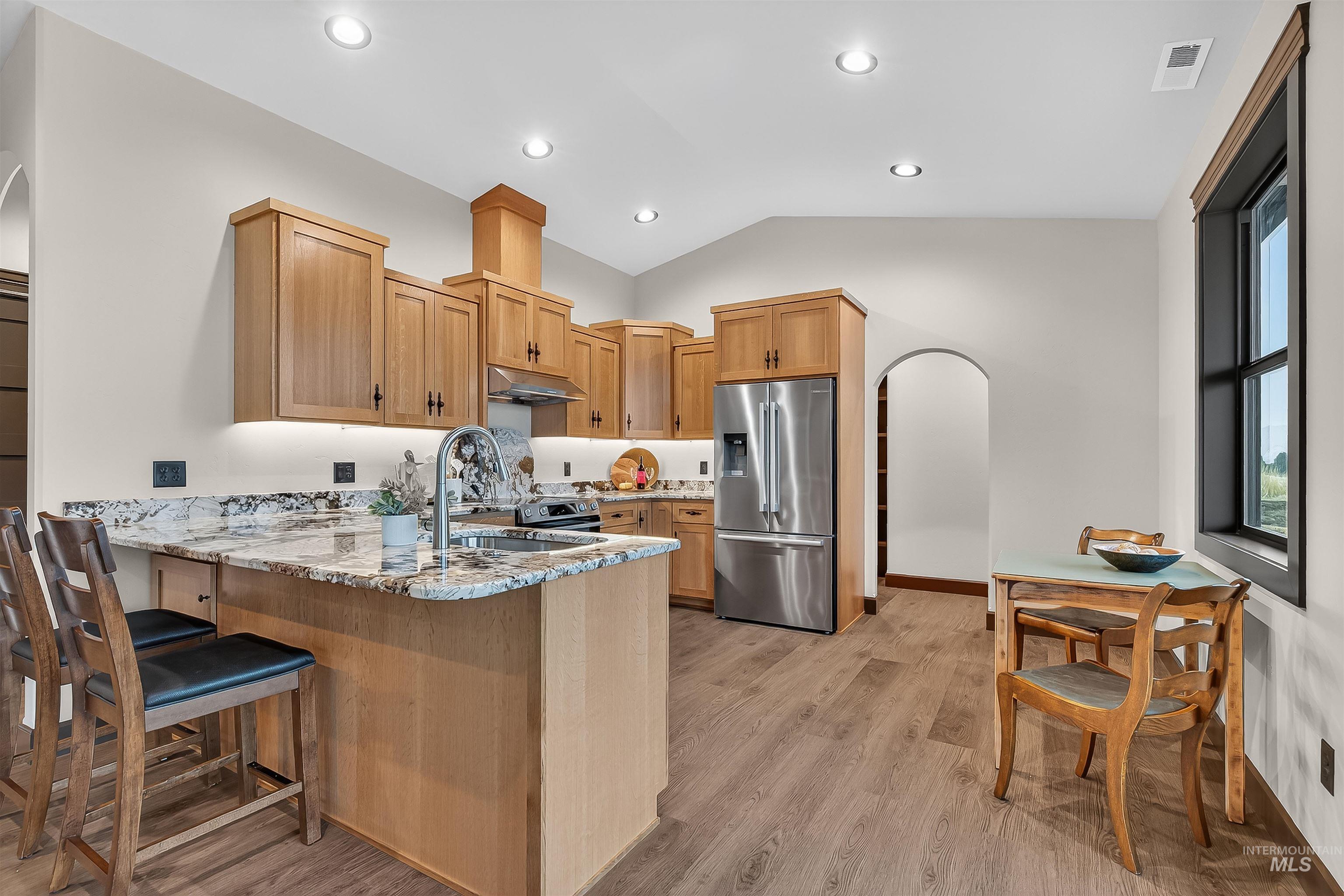 Kitchen with arched walkways, light stone counters, lofted ceiling, a peninsula, and stainless steel appliances